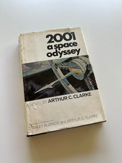 Photo of 2001: a space odyssey, the novel, with a painting of a sleek spaceship leaving a huge circular base station above Earth.