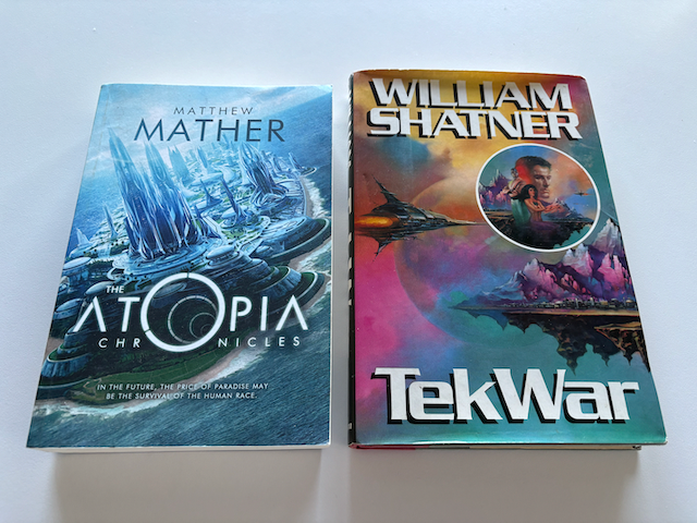 Two books on a white desk – "Atopia Chronicles" by Matthew Mather and "TekWar" by William Shatner.