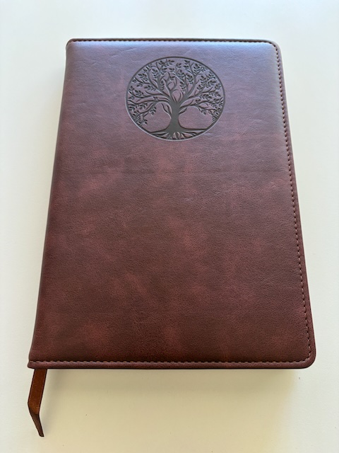 John's notebook in brown faux leather with an imprint of a tree in a circle.