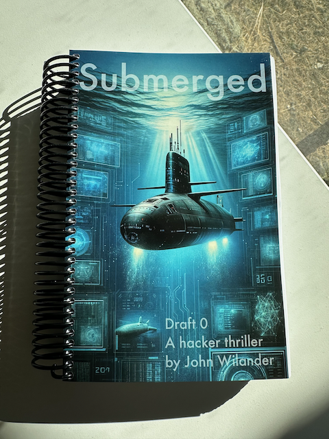Photo of Submerged, Draft 0. It's ring-bound and the cover art features a submarine just below the surface with daylight flowing down in shafts. On either side of the sub are screens with geometric shapes, several looking like spherical mesh networks.